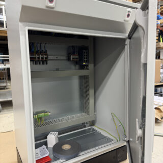 Eiskon automaatiokeskus avonaisella ovella, sisäpuolella näkyvät asennetut riviliittimet, maadoituskaapelit ja asennustarvikkeet.